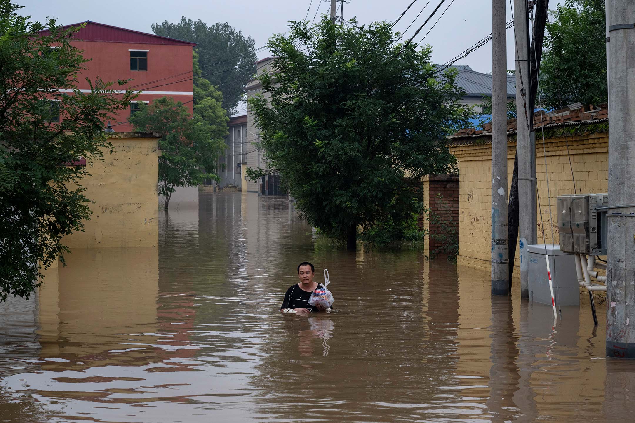 2023年8月3日，中國涿州，一名當地居民在水深及胸的洪水下，涉水走向一艘救援船。攝：Kevin Frayer/Getty Images