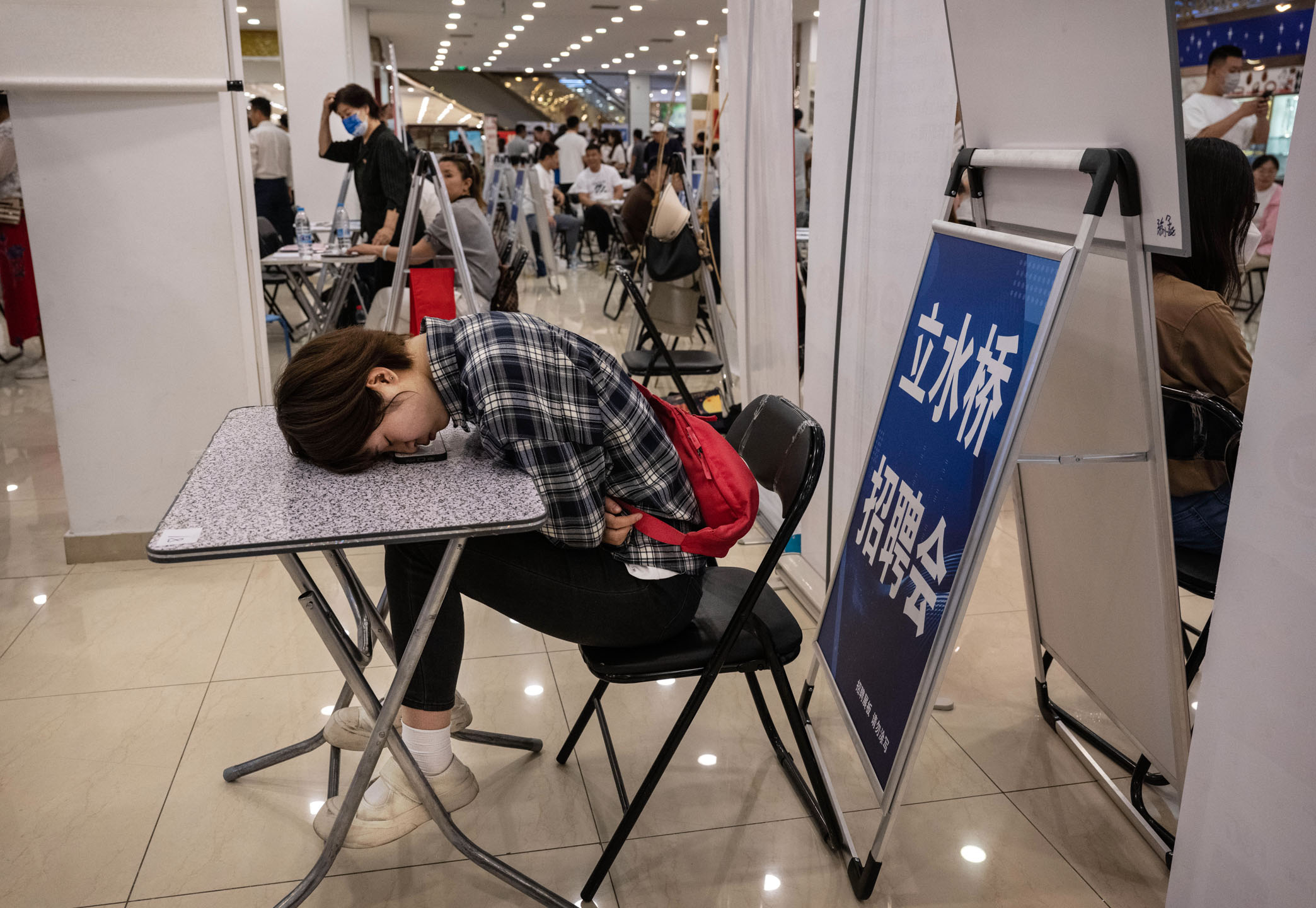 2023年6月9日，中國北京，在工作招聘會上，一名女士臥在桌子上休息。攝：Kevin Frayer/Getty Images