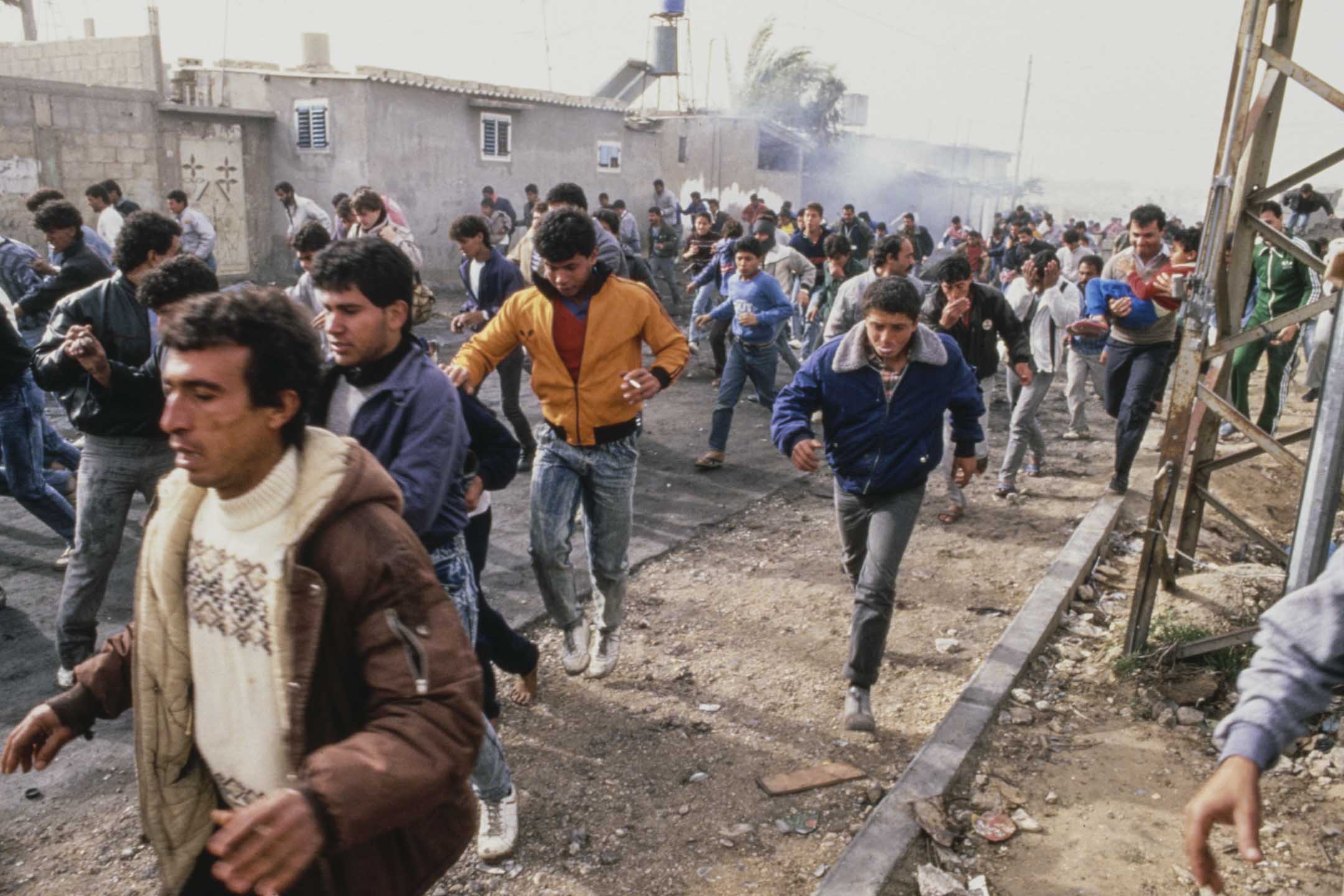 1987年12月22日，巴勒斯坦加沙，第一次巴勒斯坦起義期間，人們在街道上逃離煙霧。攝：Derek Hudson/Getty Images