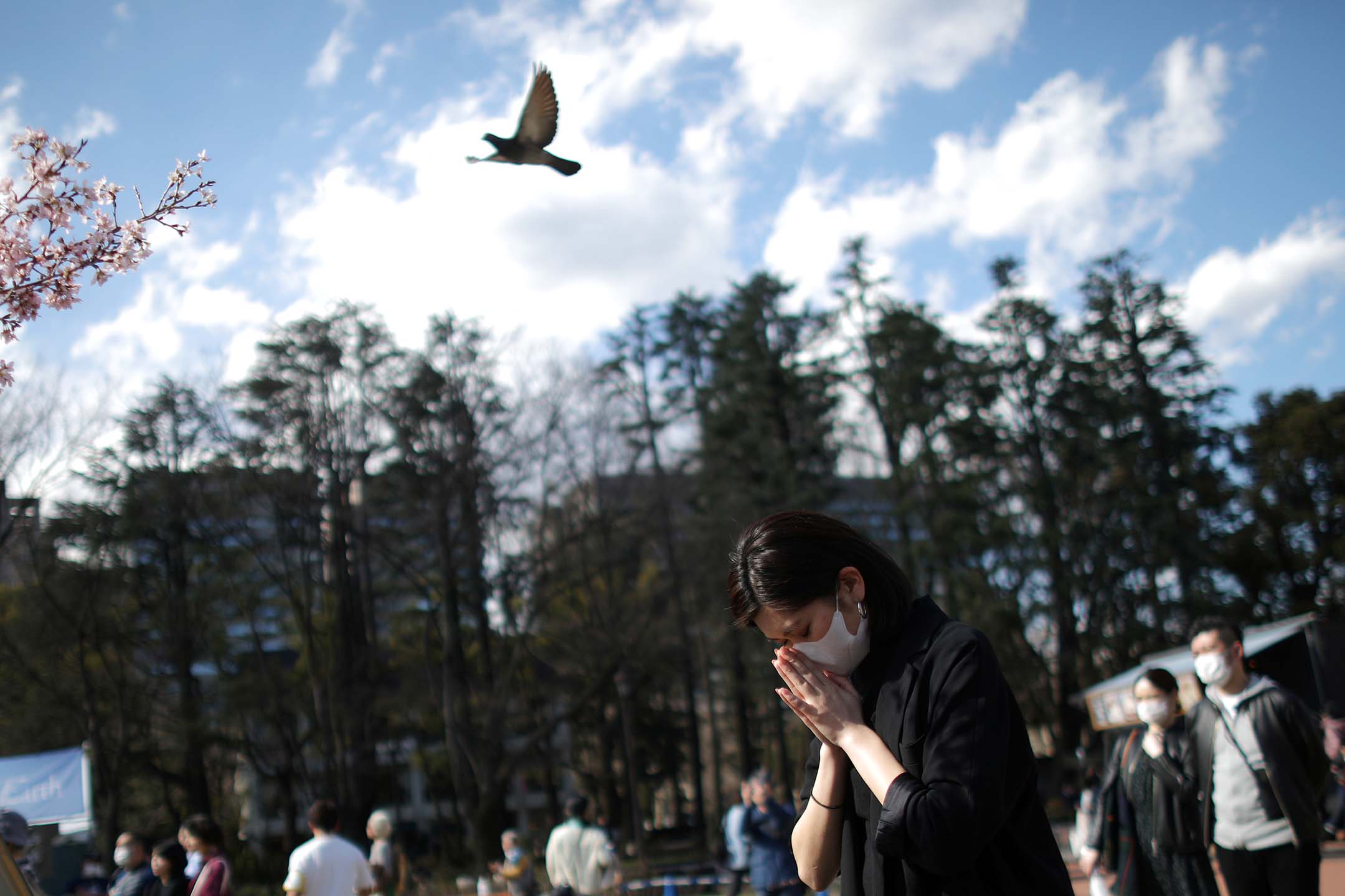 2020年3月11日,日本東京日比谷公園,一名戴著防護口罩的婦女在追悼會上祈禱。攝:Stoyan Nenov/Reuters/達志影像