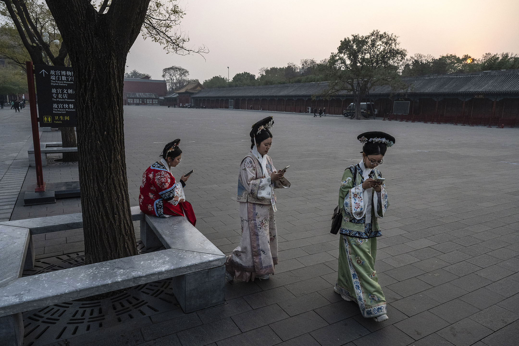 2023年11月21日,北京紫禁城外,身着清宫服装的妇女们看着手机。摄:Kevin Frayer/Getty Images