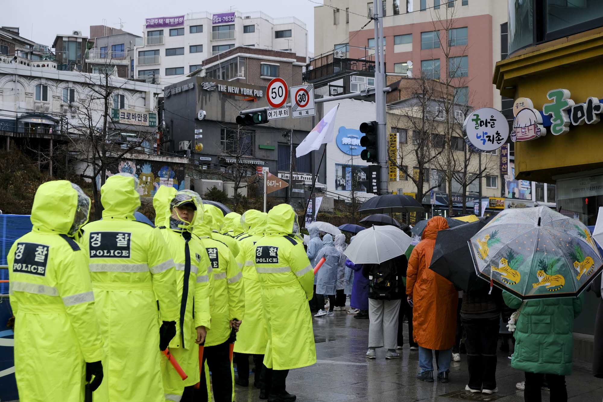 2023年12月14日,遺屬遊行到對岸的國會大樓,三十個身穿螢光背心的警員跟在家屬旁邊,形成一道警牆,阻隔他們與路上的車流。攝:余美霞/端傳媒