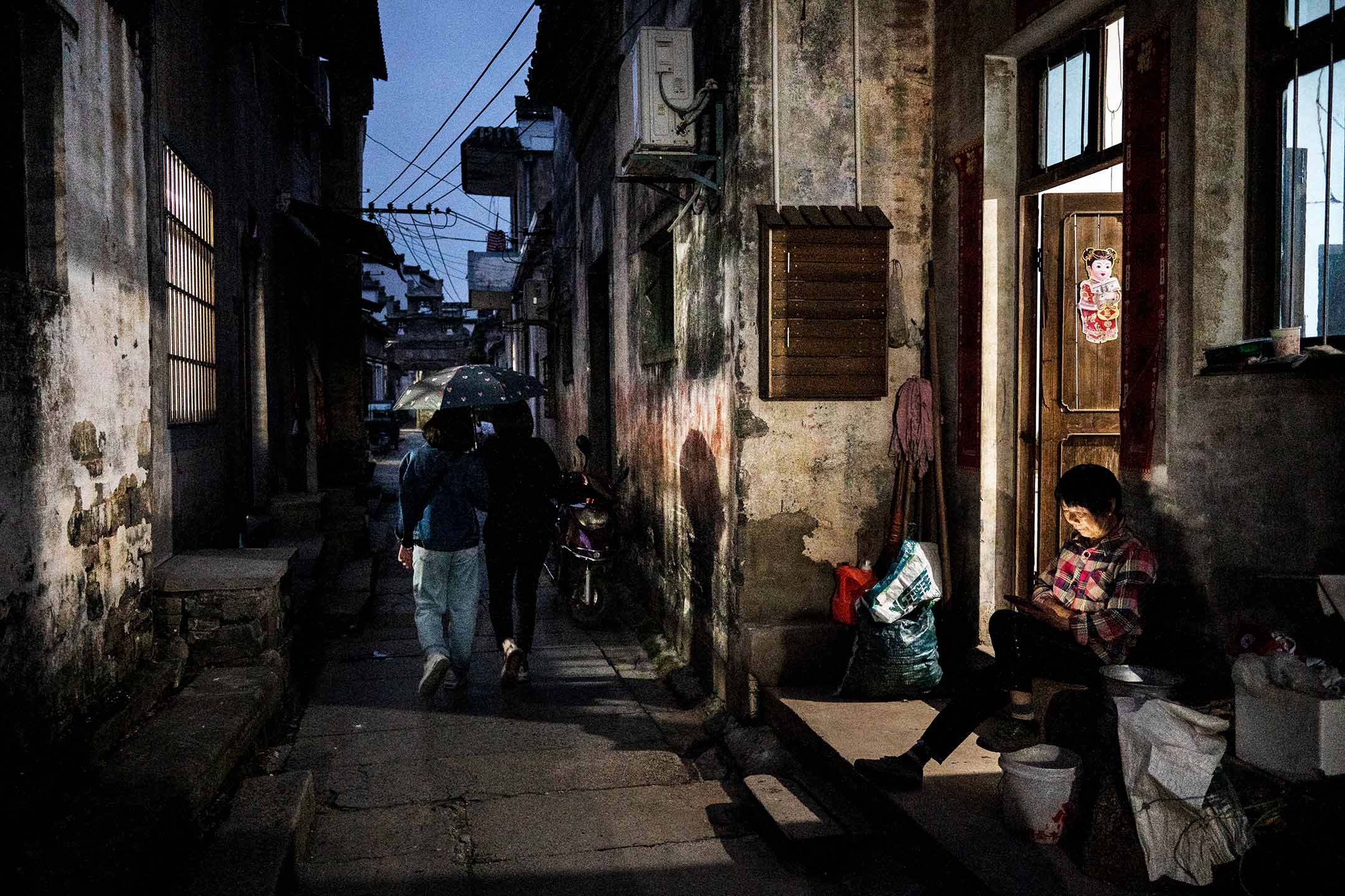 2023年5月10日,中国安徽省,一名女士坐在房子外看手机。摄:Kevin Frayer/Getty Images