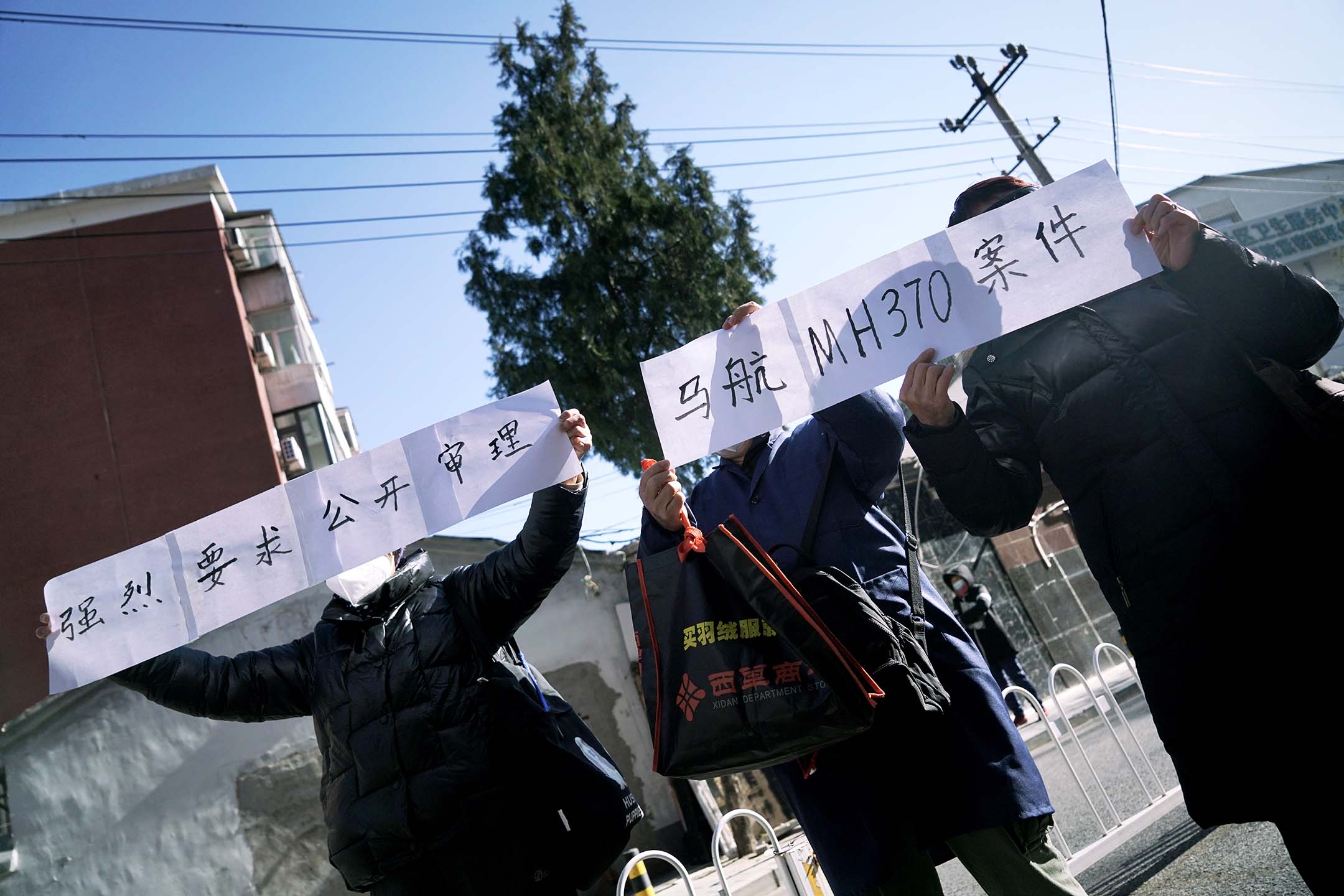 2023年11月27日,北京法院外,马航 MH370 失踪航班乘客的亲属举着牌子请愿。摄:Cai Xingzhuo/VCG via Getty Images