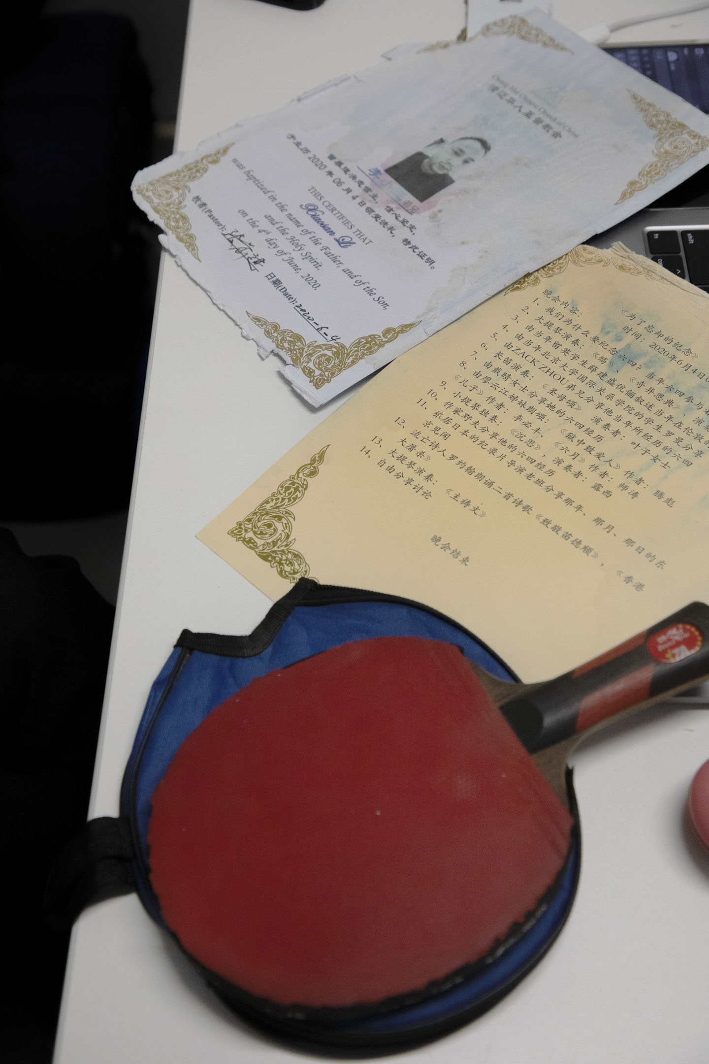 2020年6月4日李小三在泰国清迈受洗皈依基督教的受洗证书,当天教堂的纪念活动节目单和乒乓球拍是李小三一直带到纽约的唯一几件私人物品。摄:Hai Zhang/端传媒
