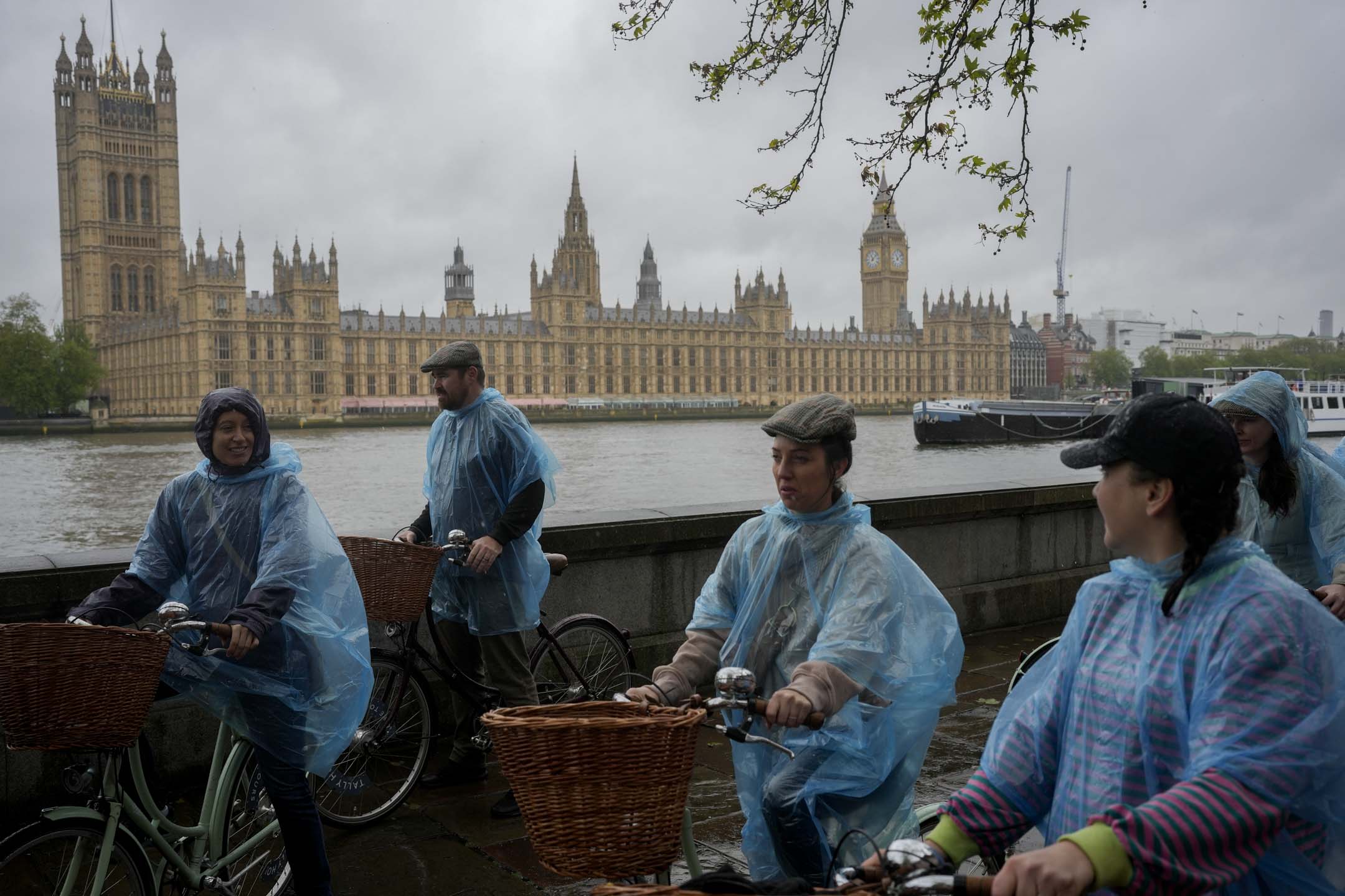 2024年5月3日,英國倫敦,遊人穿著潮濕的塑膠雨傘騎自行車遊覽議會大廈。攝:Kin Cheung/AP/達志影像