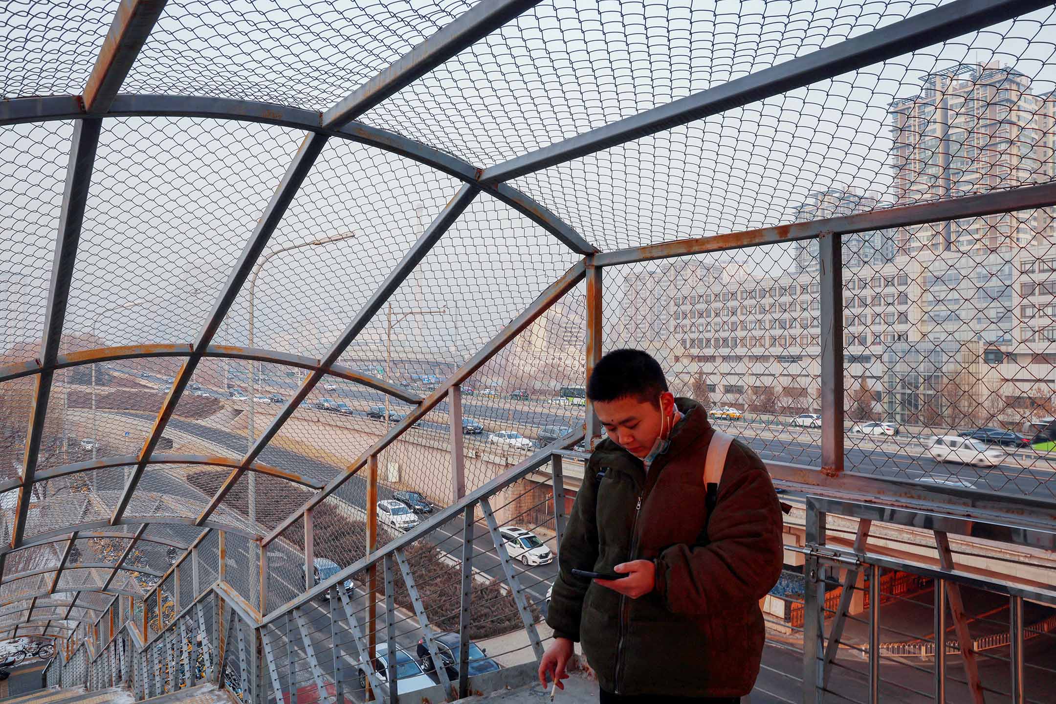 2024年1月12日,北京,一名男子在人行天橋上一邊抽煙一邊看手機。攝:Florence Lo/Reuters/達志影像