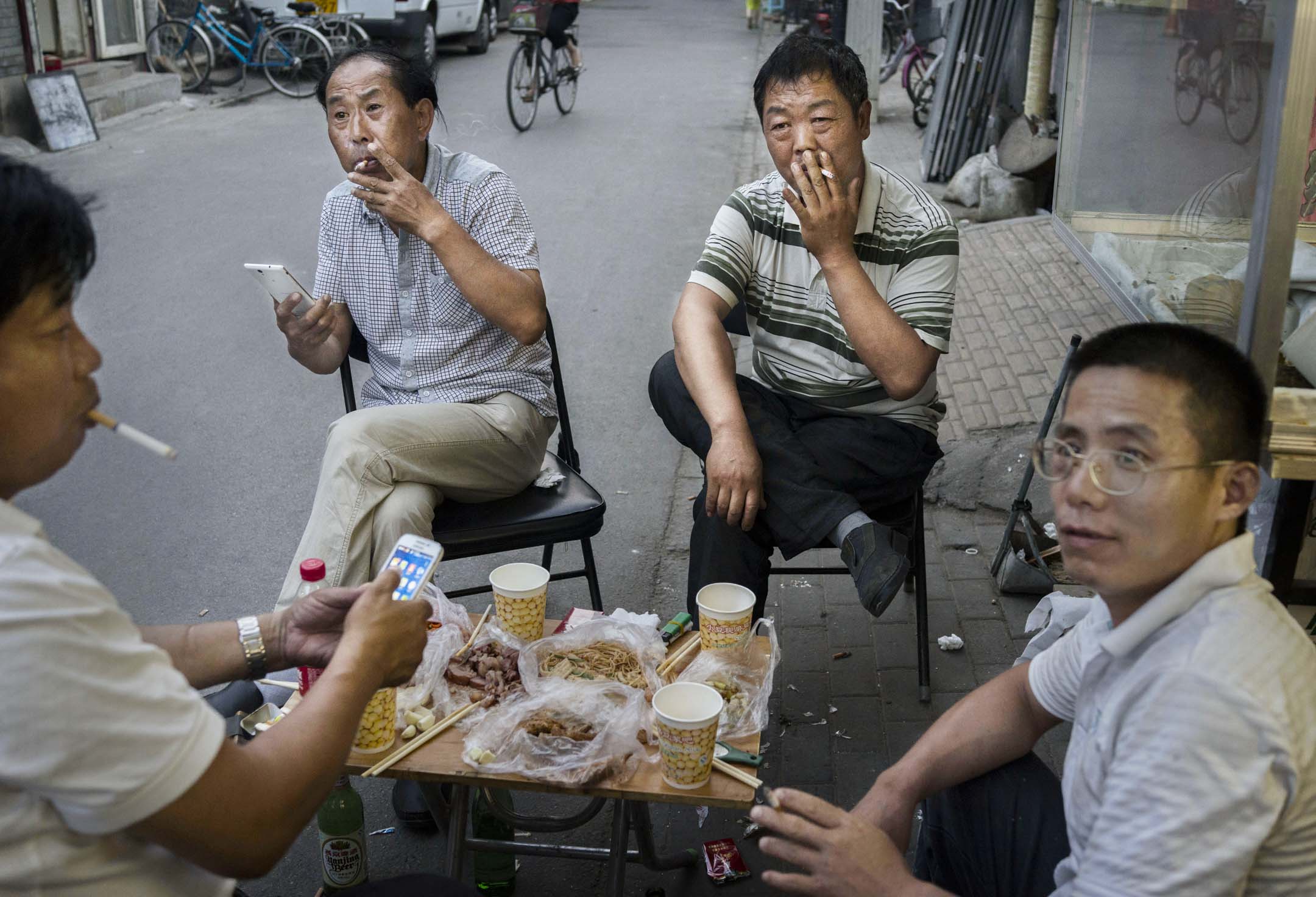 中國北京的男士在街上吃飯時一起抽煙。攝:Kevin Frayer/Getty Images
