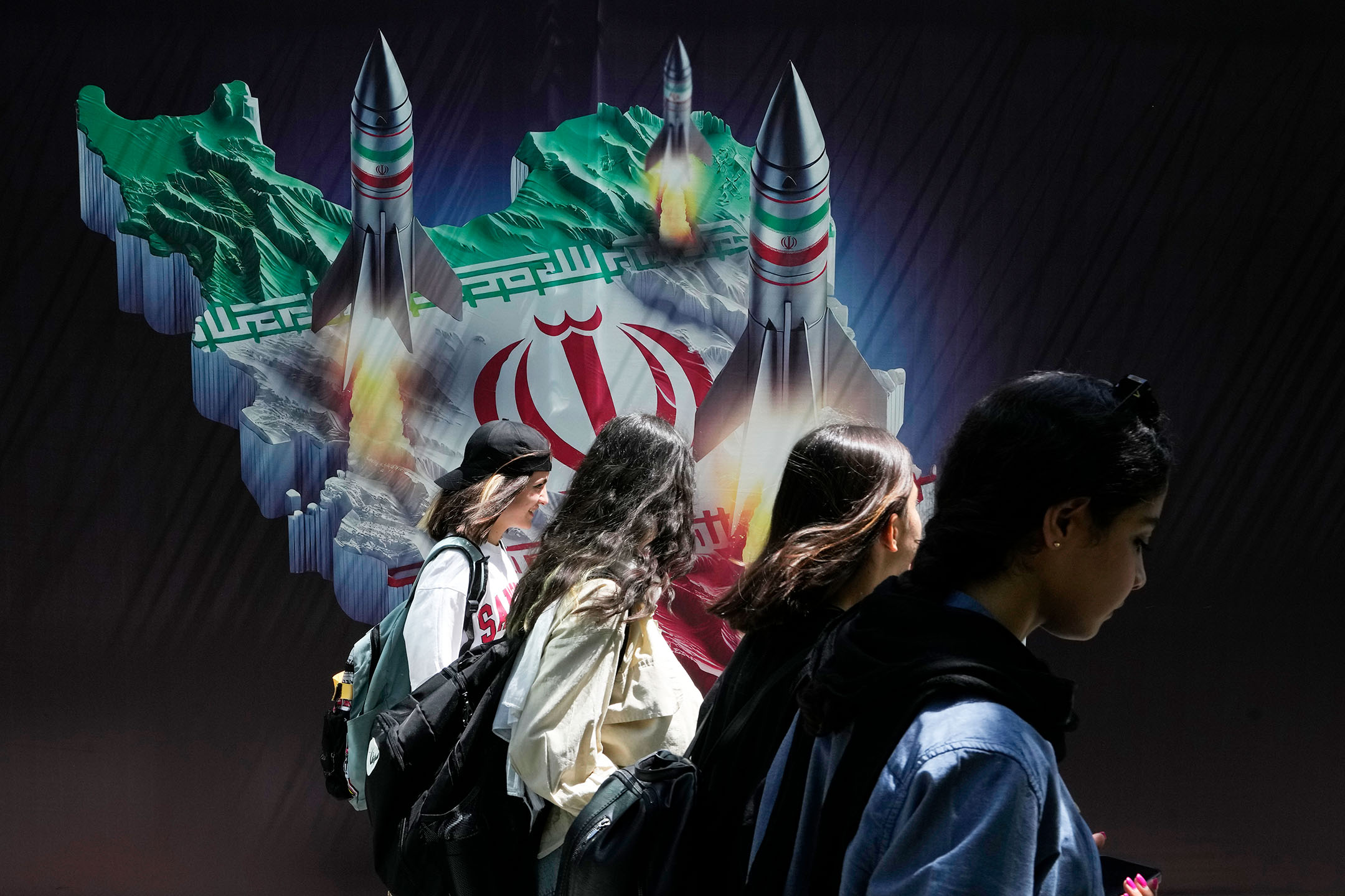 2024年4月19日,伊朗德黑蘭,伊朗女子走在街上,橫幅上面顯示從伊朗地圖上發射防空導彈。攝:Vahid Salemi/AP/達志影像