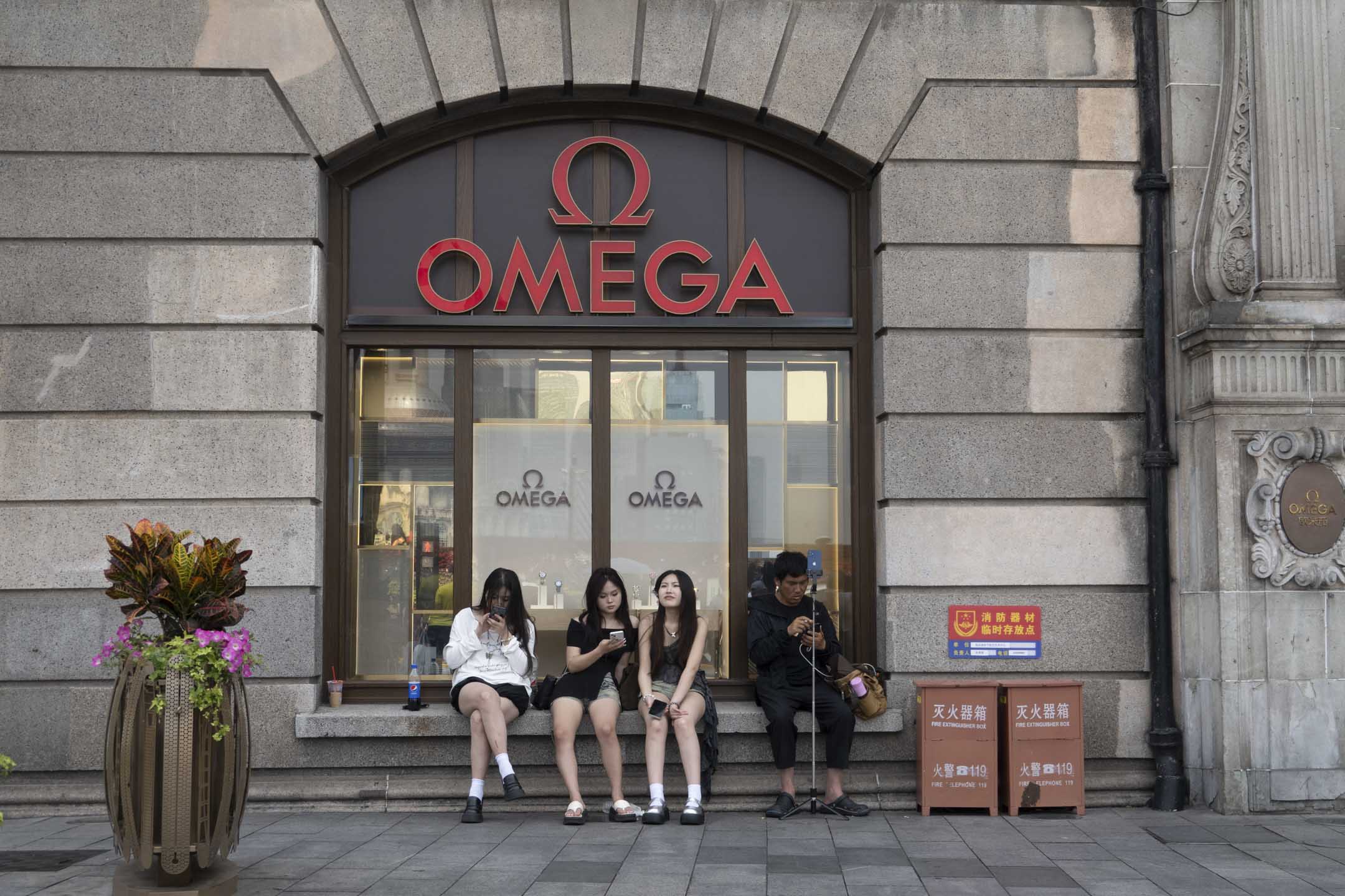 2024年6月4日,中国上海,游客坐在的 OMEGA 手表店前。摄:Costfoto/NurPhoto via Getty Images