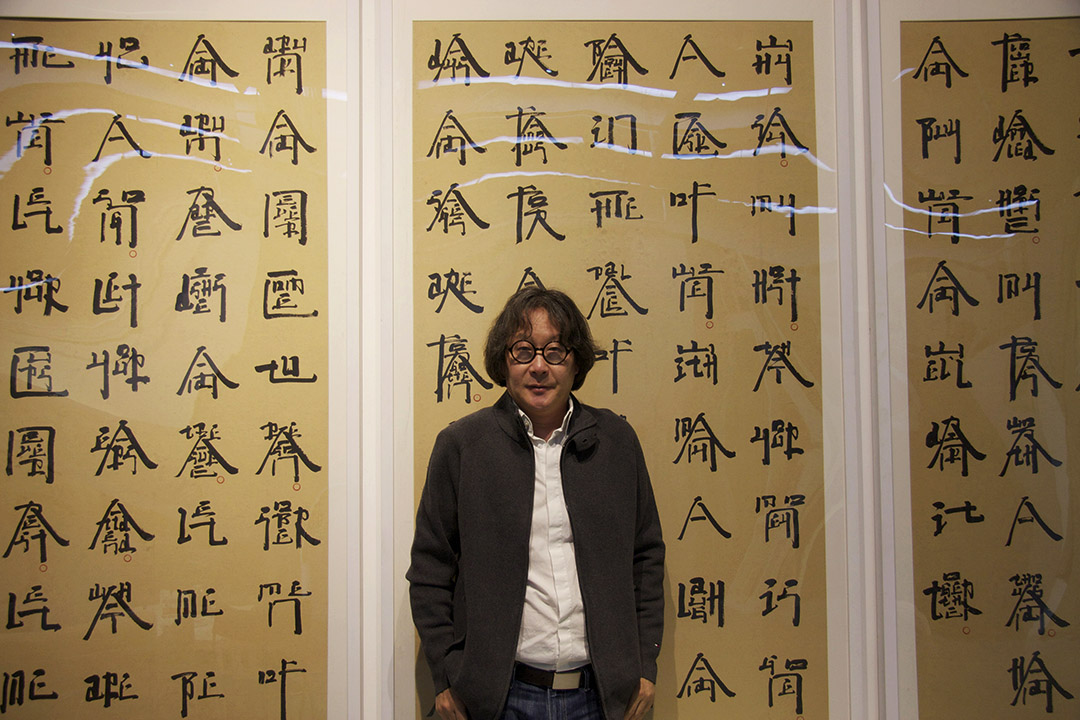 徐冰，背景是艺术家创作的《英文方块字书法》。摄：阿 Lo
