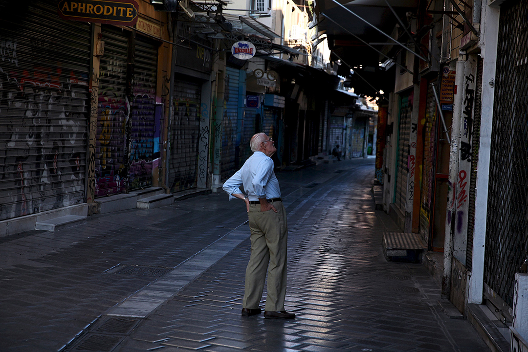 老 人 路过希腊首都雅典的商业区时驻足观看店铺的外貌。摄：Yiannis Kourtoglou/Reuters