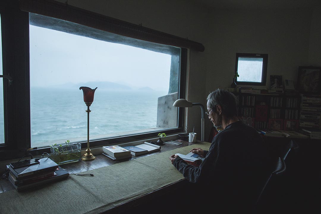 面向海邊，在書房看書的刺鳥咖啡館負責人曹以雄。攝：王嘉豪/端傳媒